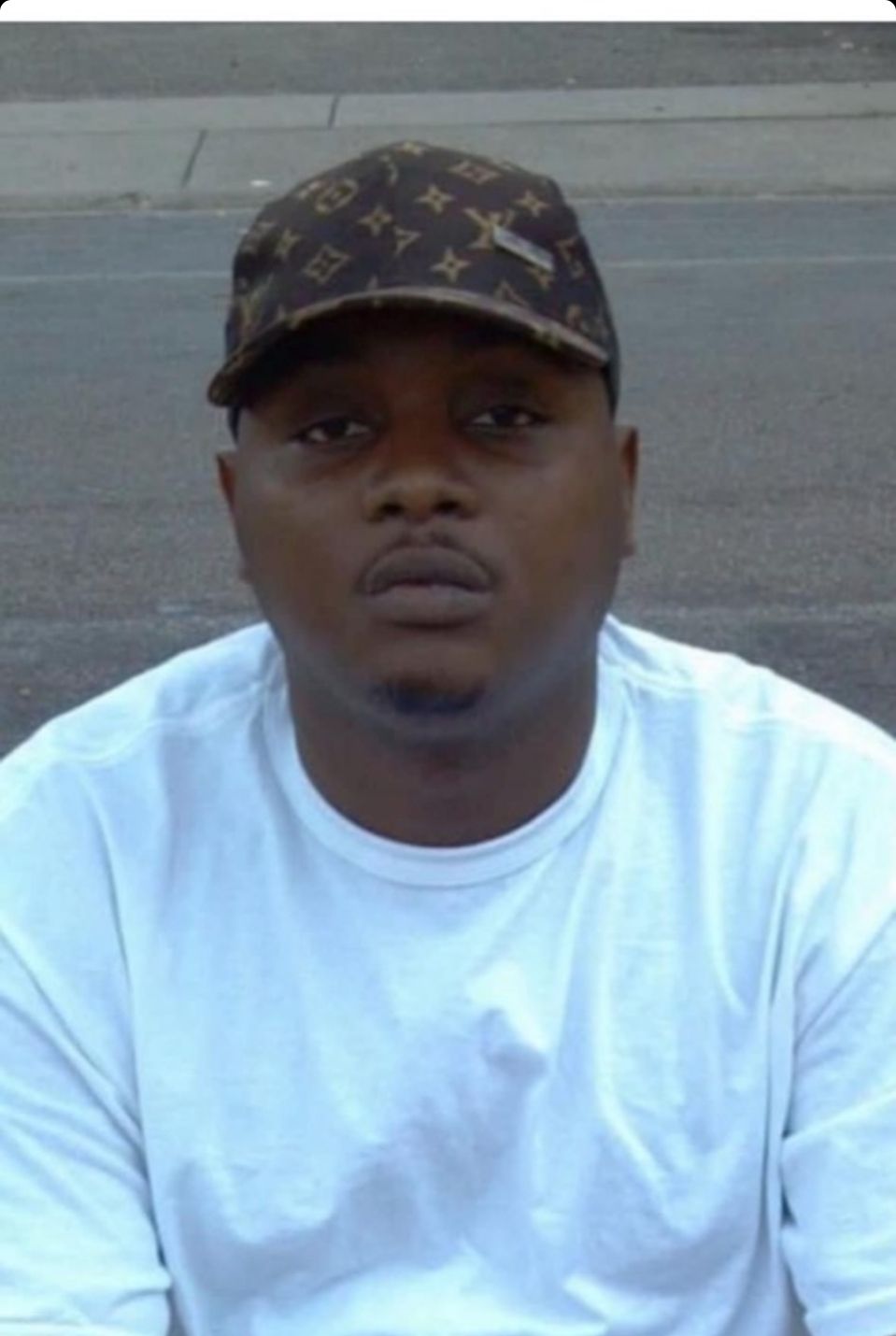 A photo shows a Black man wearing a Louis Vuitton-patterned baseball cap and a long-sleeved white T-shirt.