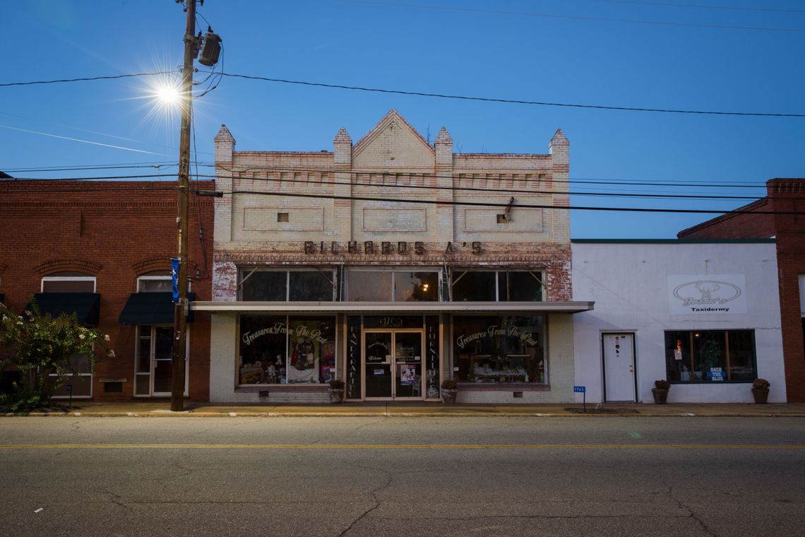 Downtown Lumpkin has a row of storefronts including a taxidermy shop, a sun-bleached gas station, and a gun store.
