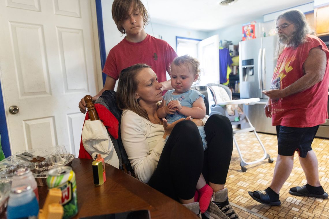 A photo of a White woman holding a crying baby girl while sitting at a kitchen table.