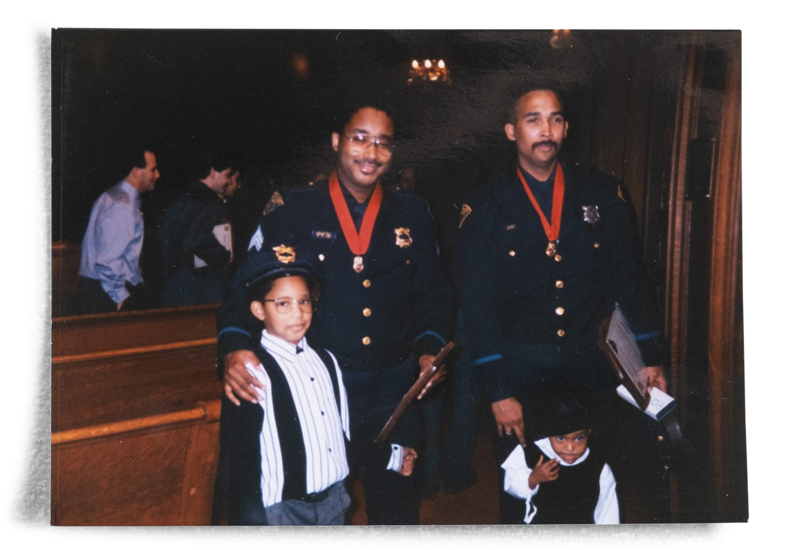 Wilbert L. Cooper as a child, standing next to his father and his father’s police partner, both wearing medals around their necks. 