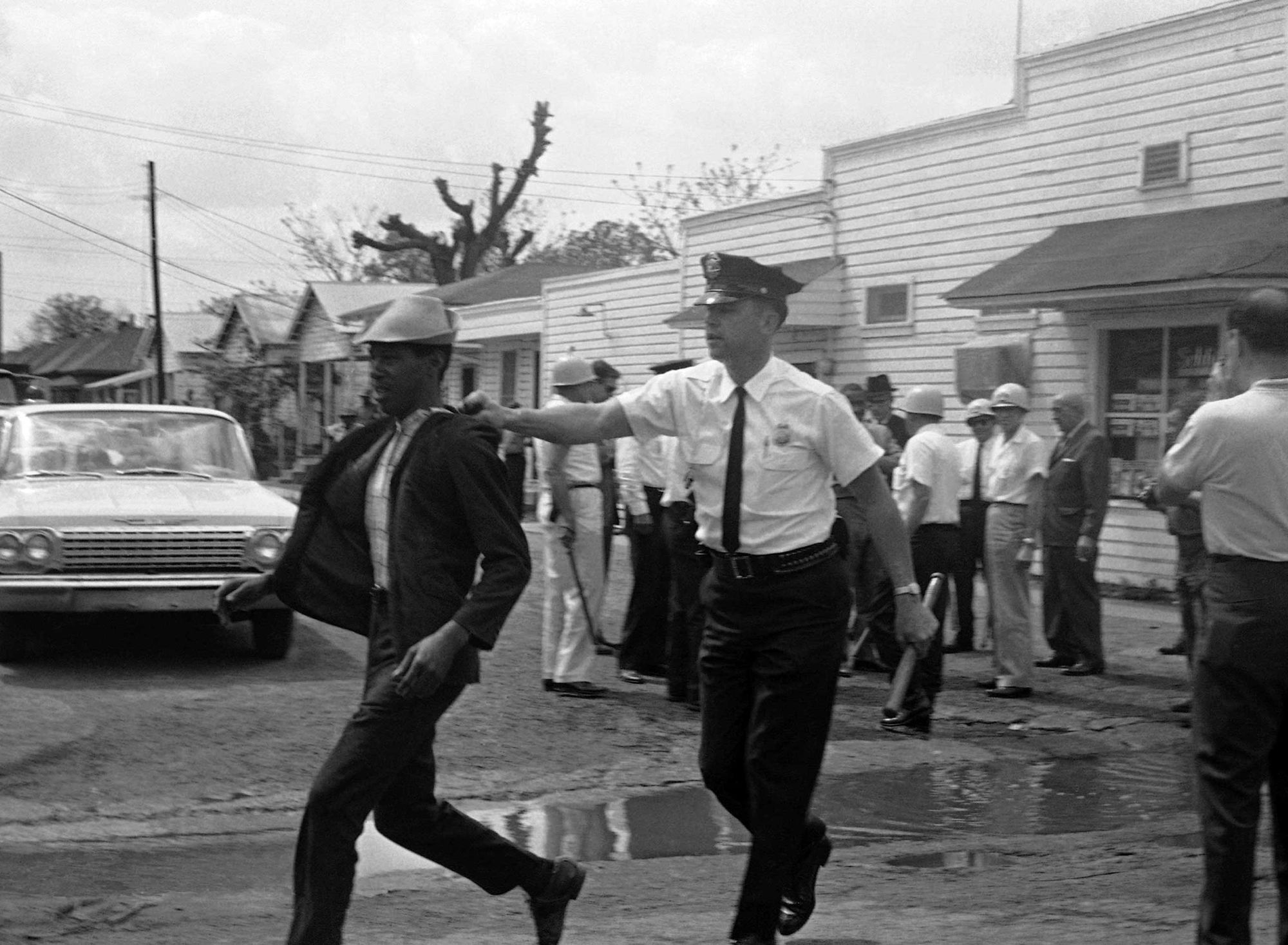A black-and-white photo shows a White police officer grabbing a younger Black man.