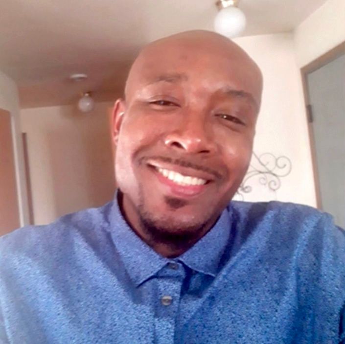 A portrait shot of a Black man wearing a blue button-up shirt.