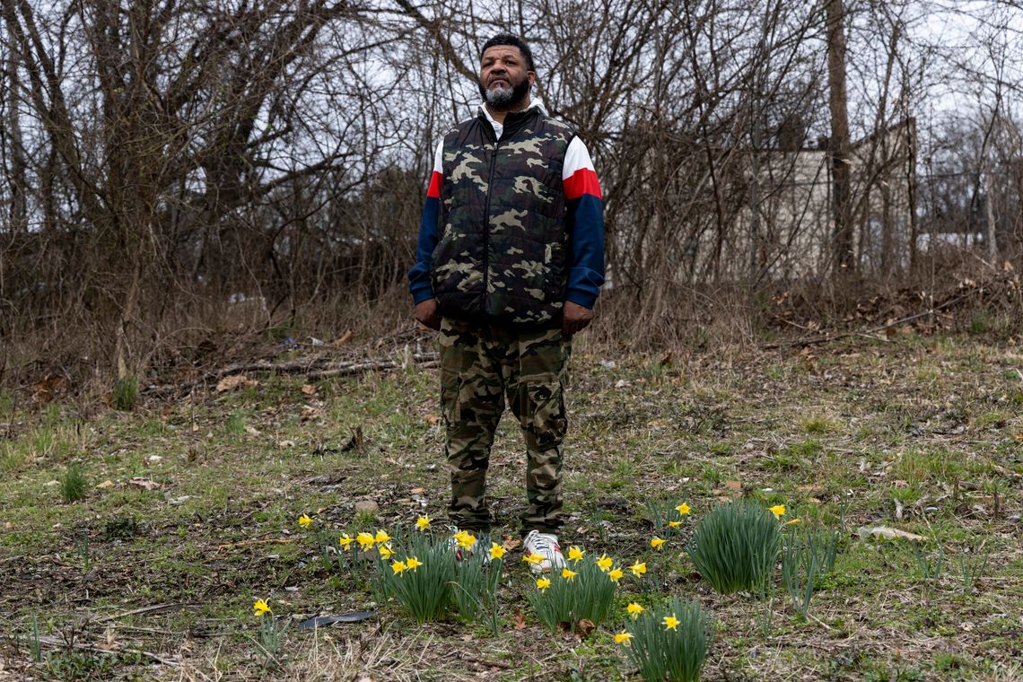 Reginald Monroe, a Black man, stands in a field with flowers blooming at his feet. 