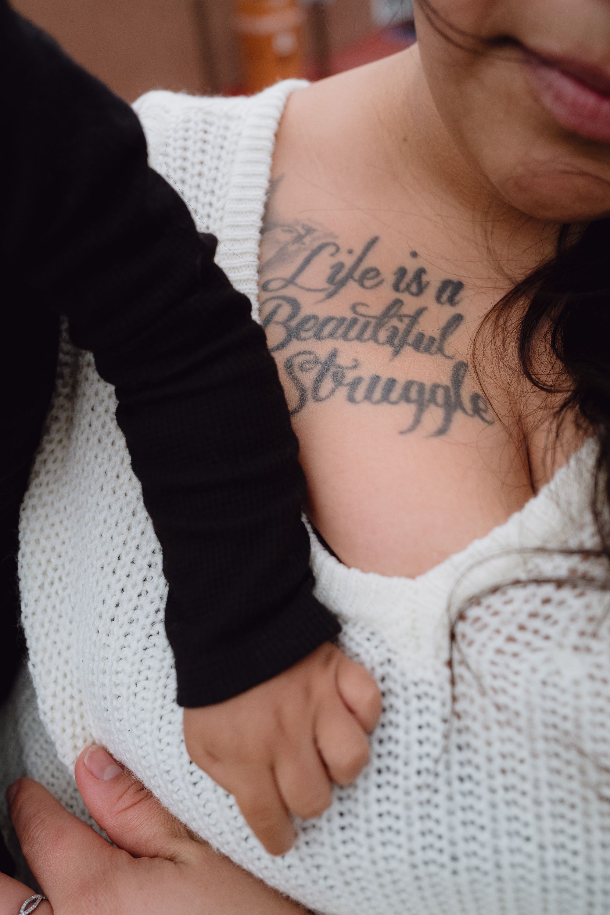 A closeup photo of Mapes shows a tattoo in script that reads: “Life is a Beautiful Struggle” on her chest. Her infant son’s arm is resting on her chest. 