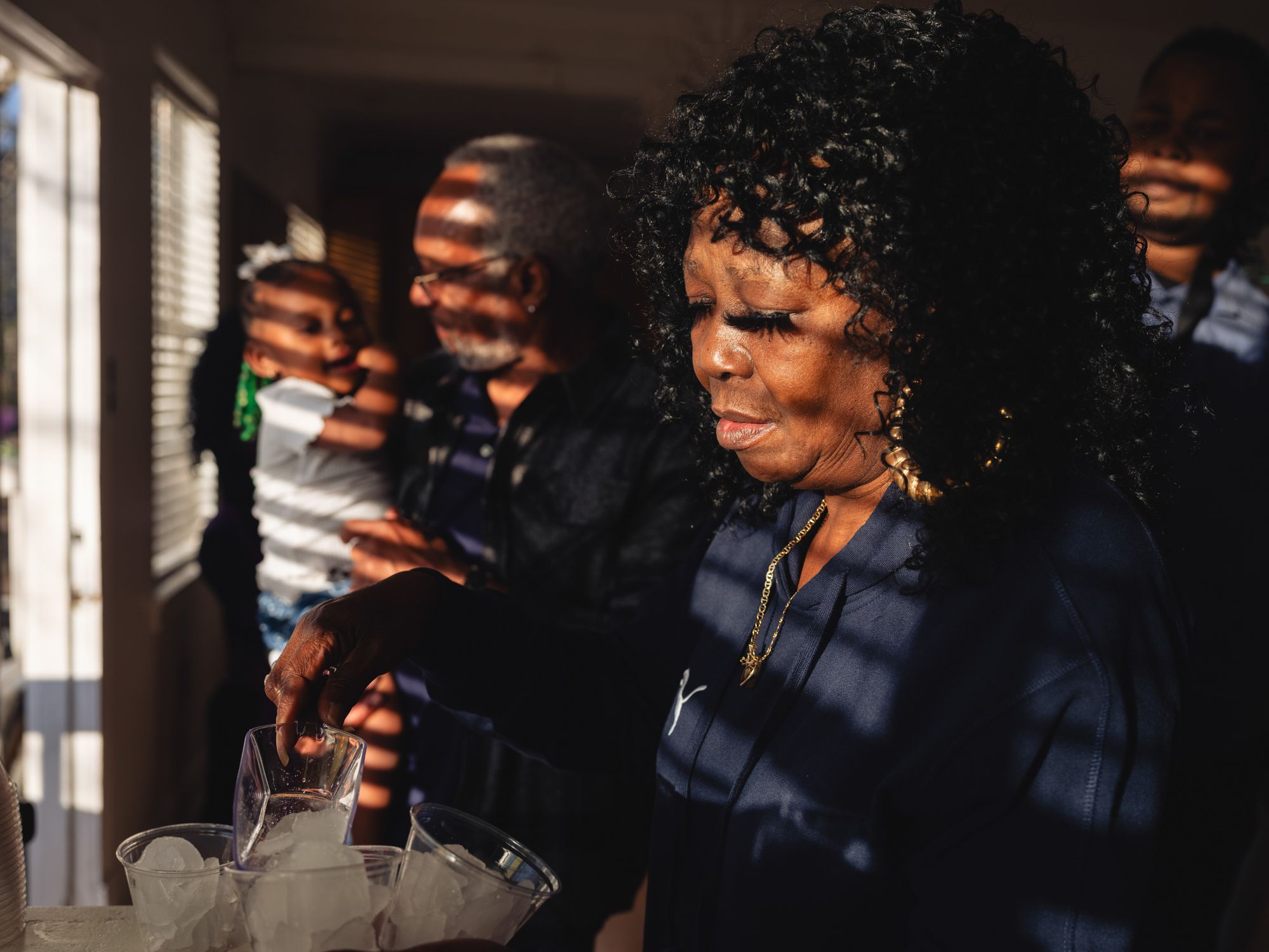 As sunlight falls on their faces through blinds, Armour puts ice in cups while Moses carries her great-niece.
