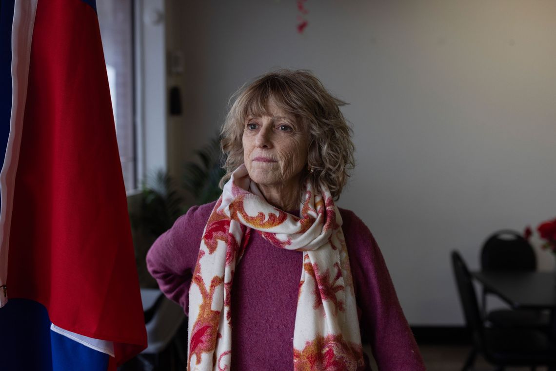 A photo of a White woman with blond hair looking off camera while standing next to a Haitian flag. 