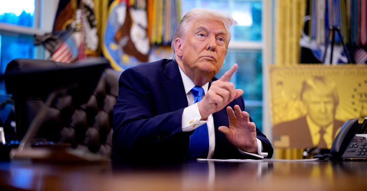 Trump, a White man in a navy suit and a blue tie, is looking outward, pointing at a person while sitting in the Oval Office. 