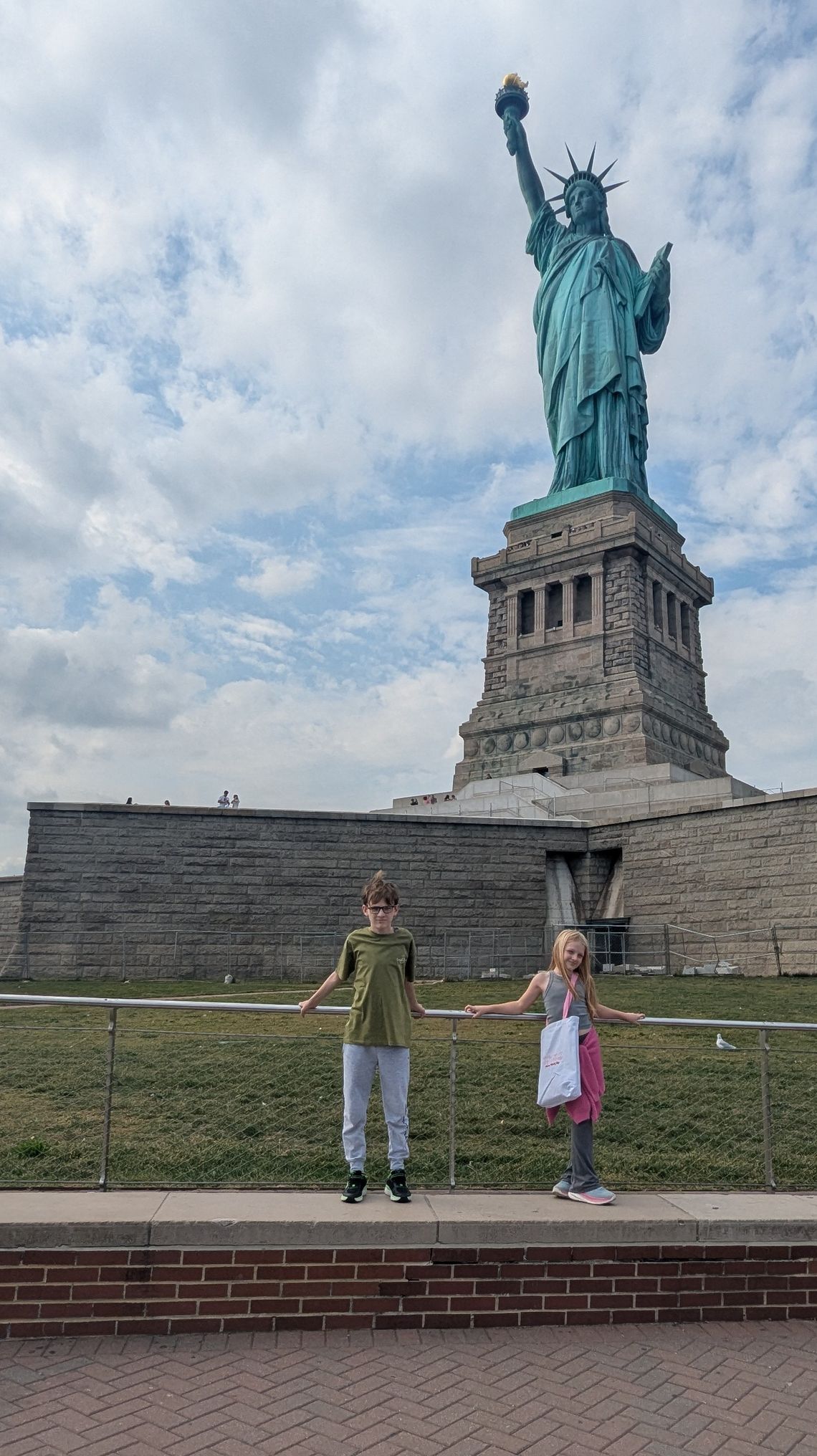 A photo shows two children standing in front of the Statue of Liberty.
