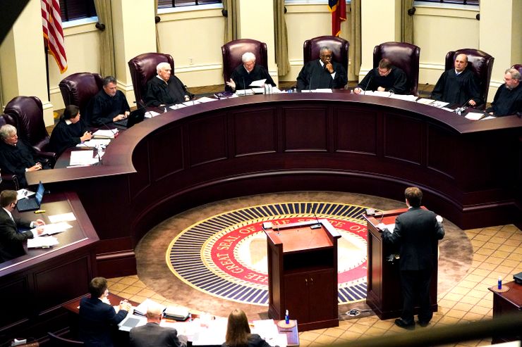 A group of Supreme Court justices sitting at a raised bench while an attorney speaks at a podium. 