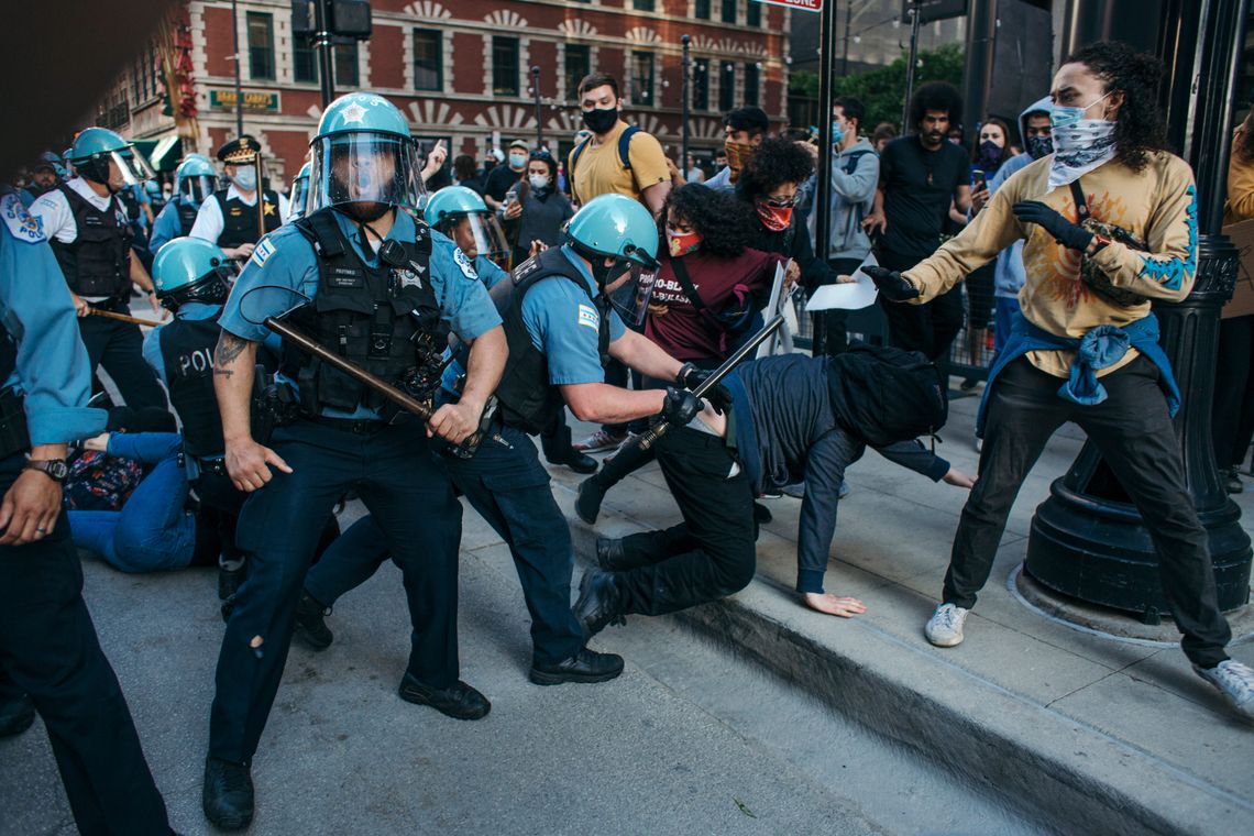 A color photo shows police with batons and face shields clashing with masked protesters.