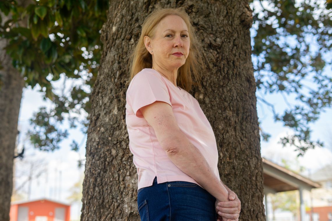 A photo shows Terri McGuire Mollica, a White woman with long blonde hair, standing in front of a tree. She is wearing a pink T-shirt and jeans.