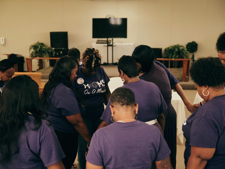 A color photo shows a group of Black women in a circle of healing inside the Williams Memorial CME Temple.