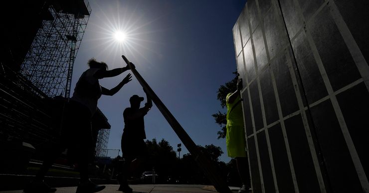 A photo shows the sun beaming above silhouettes of two people holding a board while another person constructs a wall of a makeshift prison cell. 