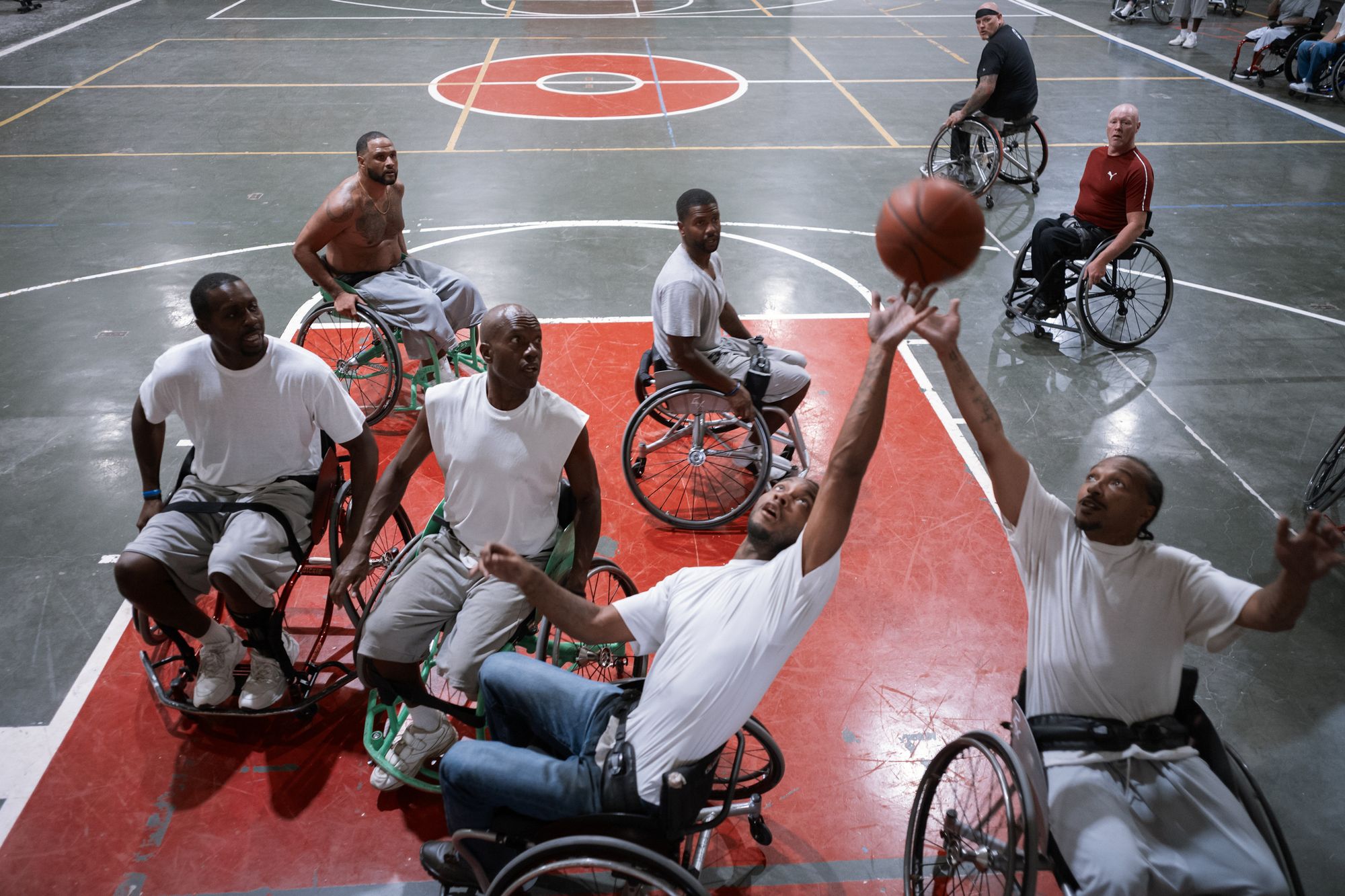 A photo shows a group of men playing wheelchair basketball. The skintones of the men range from dark-toned to light-toned. 