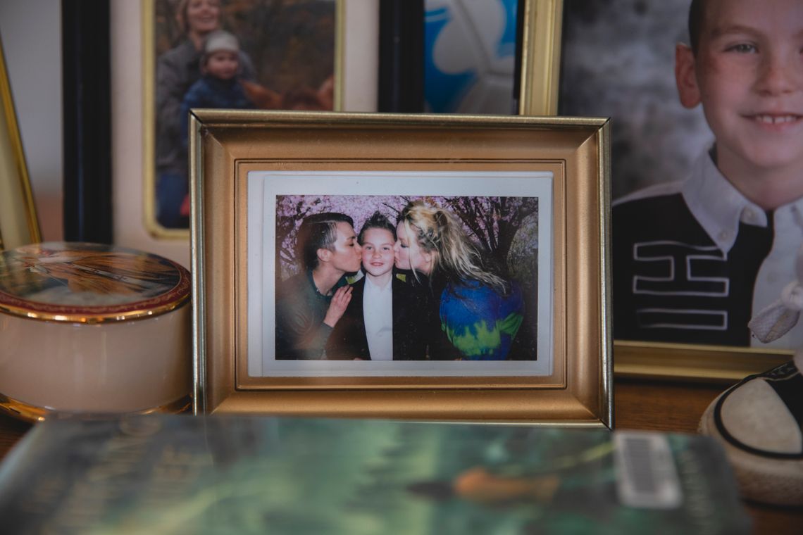 Julius, wearing a black jacket and white shirt, is kissed on the cheeks by his mothers in a framed photo sitting on a mantlepiece at their home.