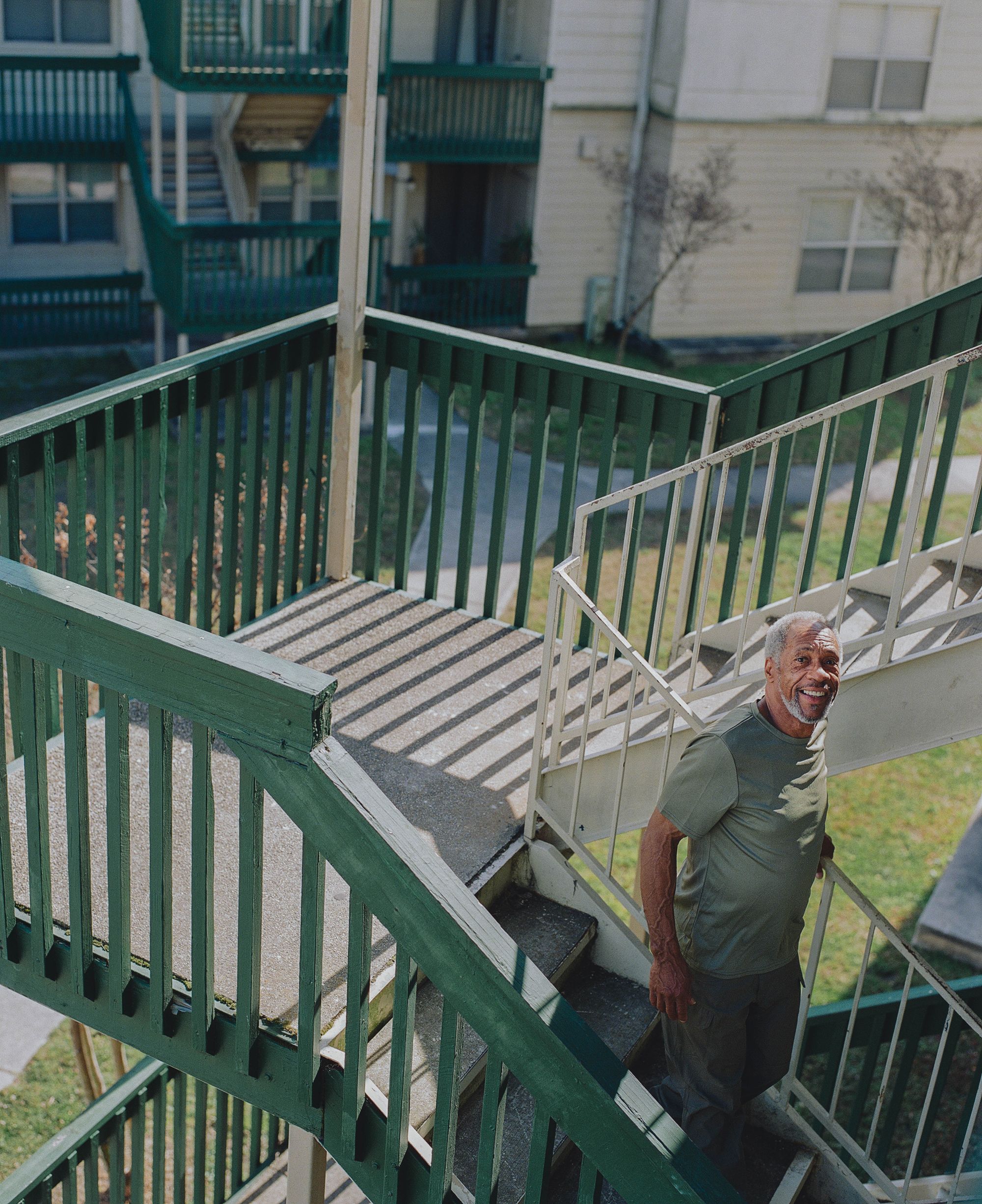 Moses, a Black man, walks down a staircase with a green railing while smiling.