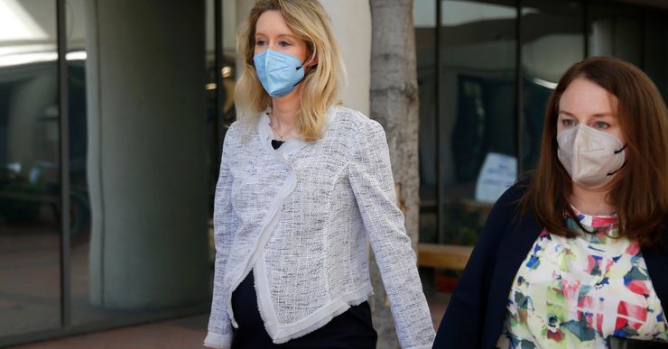 Elizabeth Holmes, a White woman with blonde hair, is visibly pregnant and walking with a female member of her defense team in a photo.  