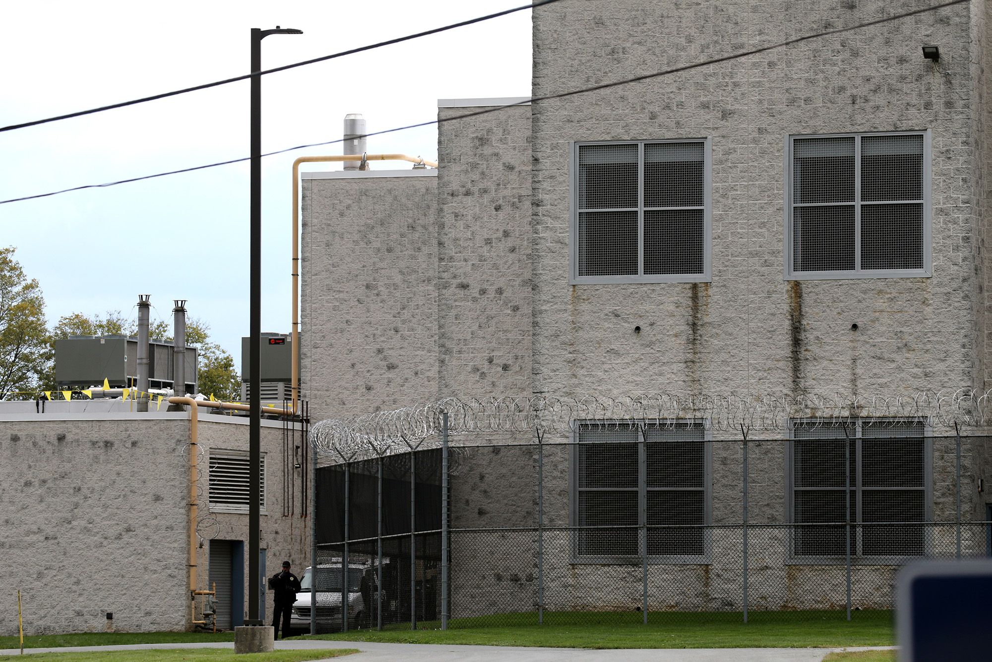A photo shows a gray brick prison building surrounded by barbed wire fencing. 
