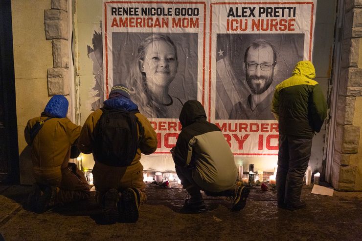 A photo shows four people kneeling and standing as they place candles against a wall. Two posters on the wall show images of a White woman and a White man with text that reads, "Renee Nicole Good, American mom," "Alex Pretti, ICU nurse," and "murdered by ICE."  