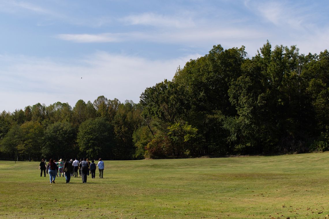 A photo of a group of people walking on a mowed lawn toward a forest.