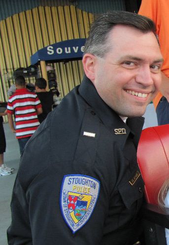 A White man in a police uniform smiles at the camera. 