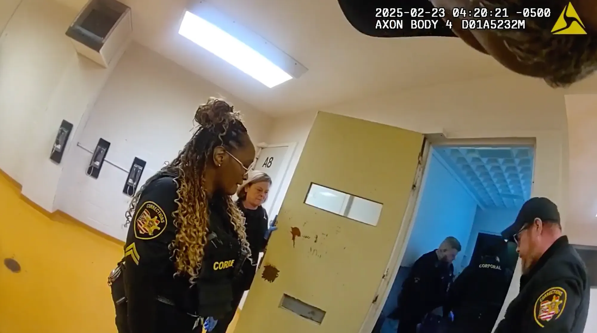 A still image from a body camera shows Jennifer Wade’s cell with three corrections officers standing outside and two standing inside. Her body is not visible. 