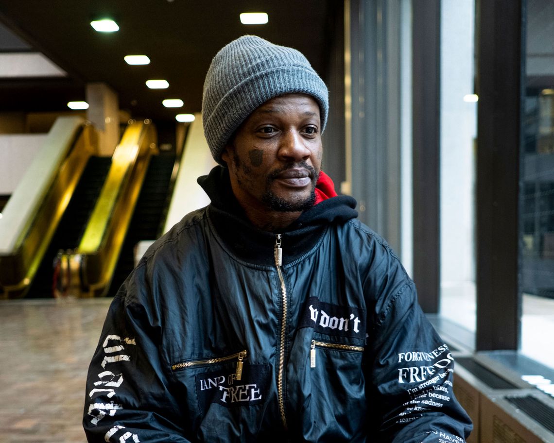 A Black man in a gray beanie poses for a portrait by a window in the lobby of the Cuyahoga County Justice Center.