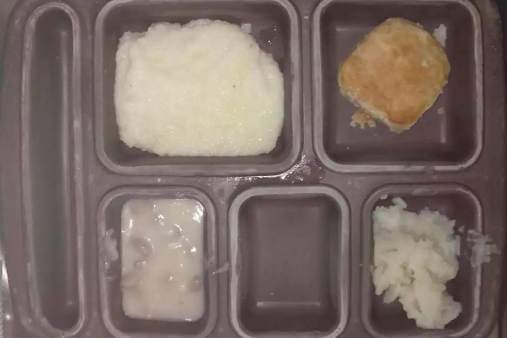 A dark gray colored food tray contains compartments with mashed potatoes, a biscuit, and some gravy. 