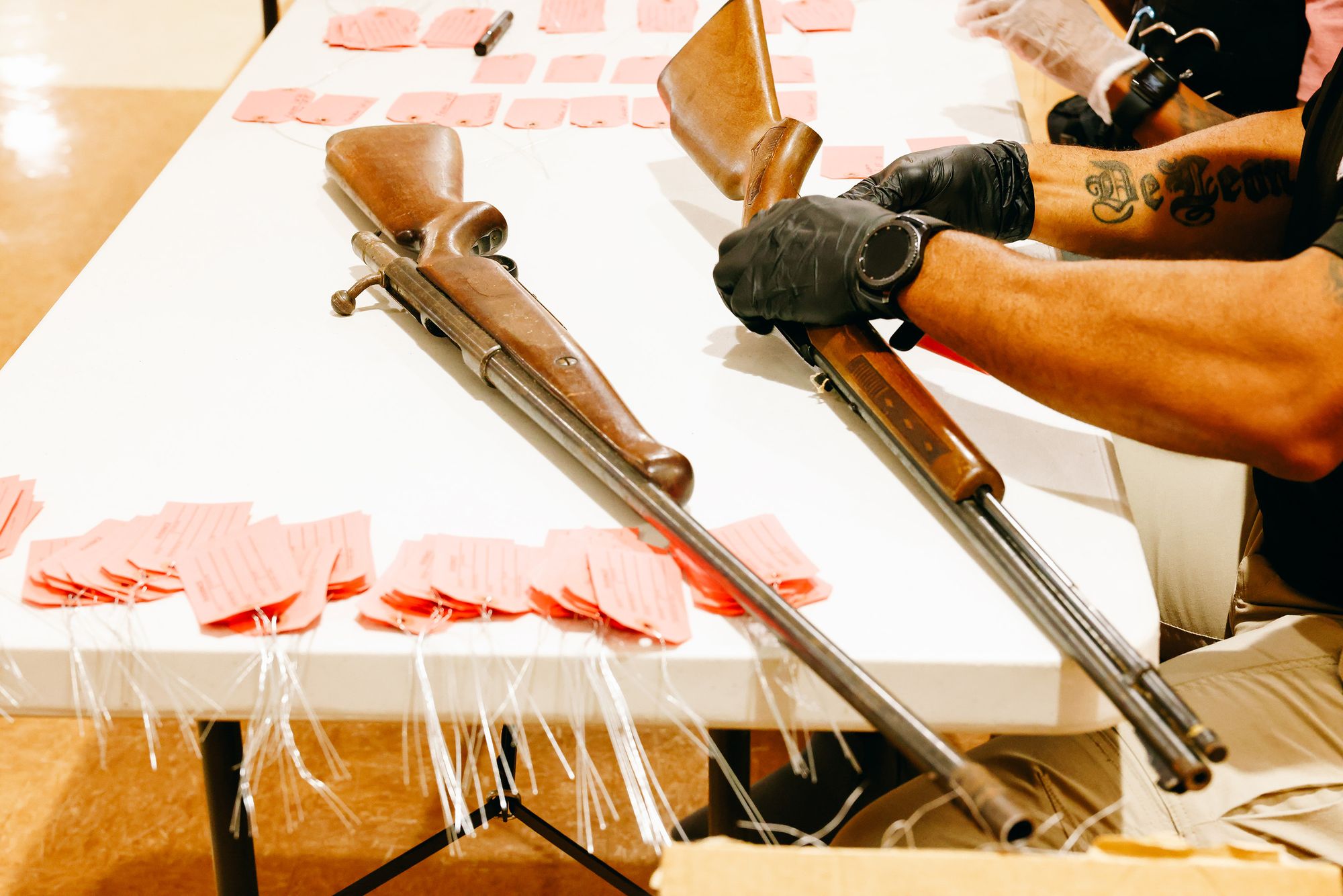 An officer inspects one of the two long guns on a table. 
