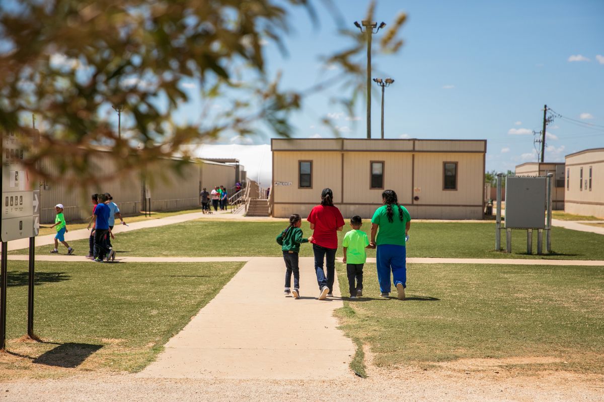 A photo shows four people, including two children, walking toward a complex of tan, one-story buildings. 