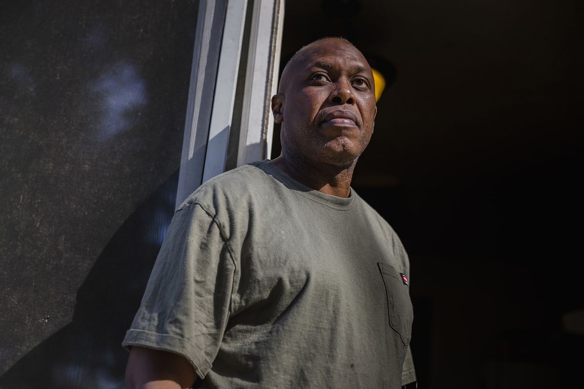 A Black man, wearing a jade green T-shirt, stands in front of a sliding door.
