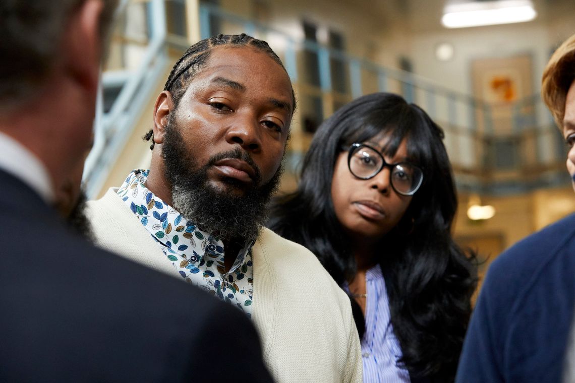 Ofonzo Staton, a Black man with cornrows and a beard and goatee, wears a cream-colored cardigan and stands next to Mary Williams, a Black woman with dark rimmed glasses, medium-length hair and a navy blue suit jacket. Two other people are partially visible in the photo.