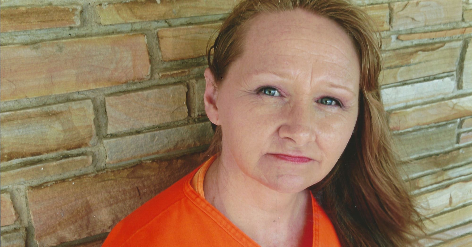 A White woman with long brown hair wears an orange shirt.  