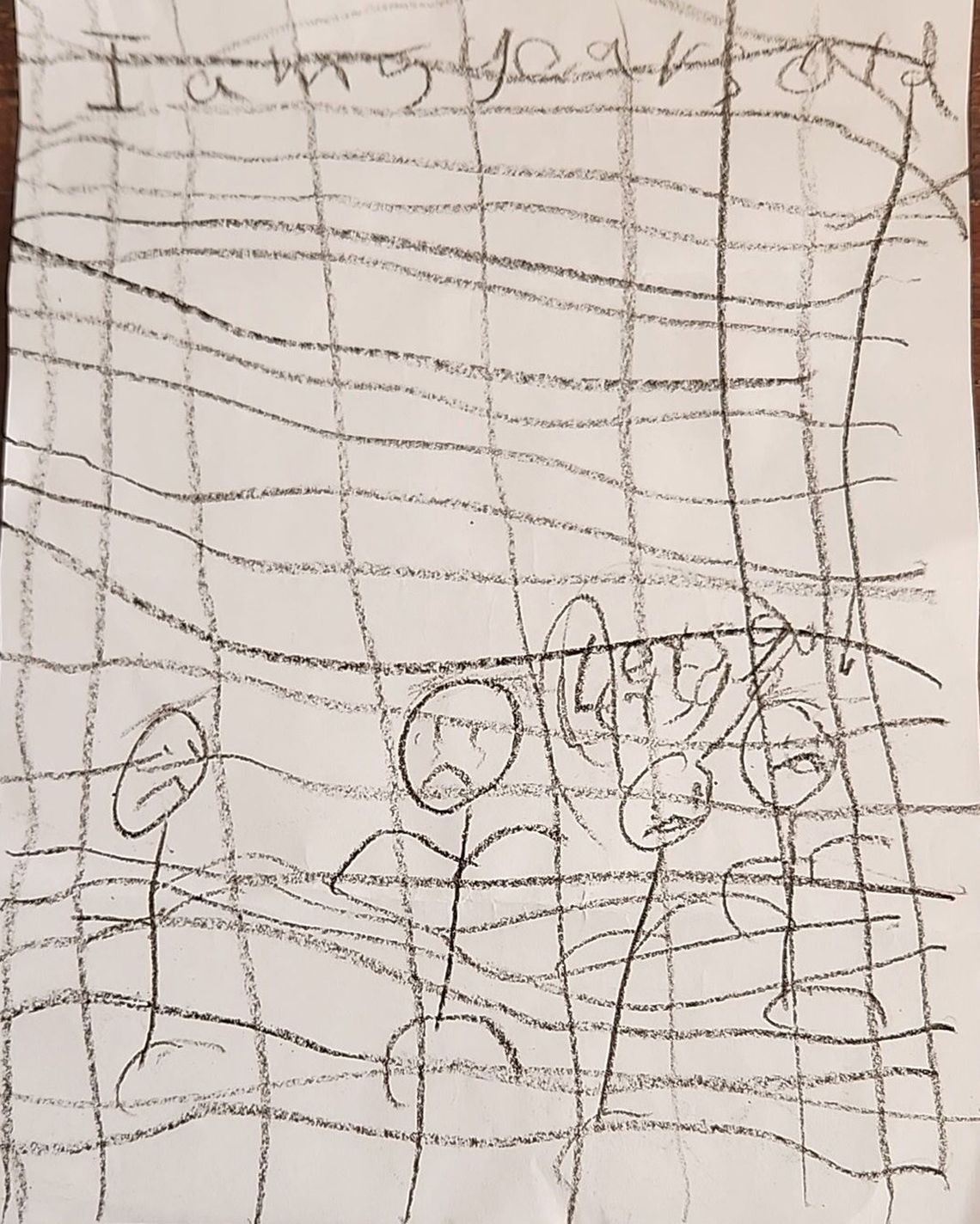 A photo of a child’s stick figure drawing showing four people behind bars. The words “I am 5 years old” are at the top of the page. Lower down, next to the figures, are the words “let us go.”