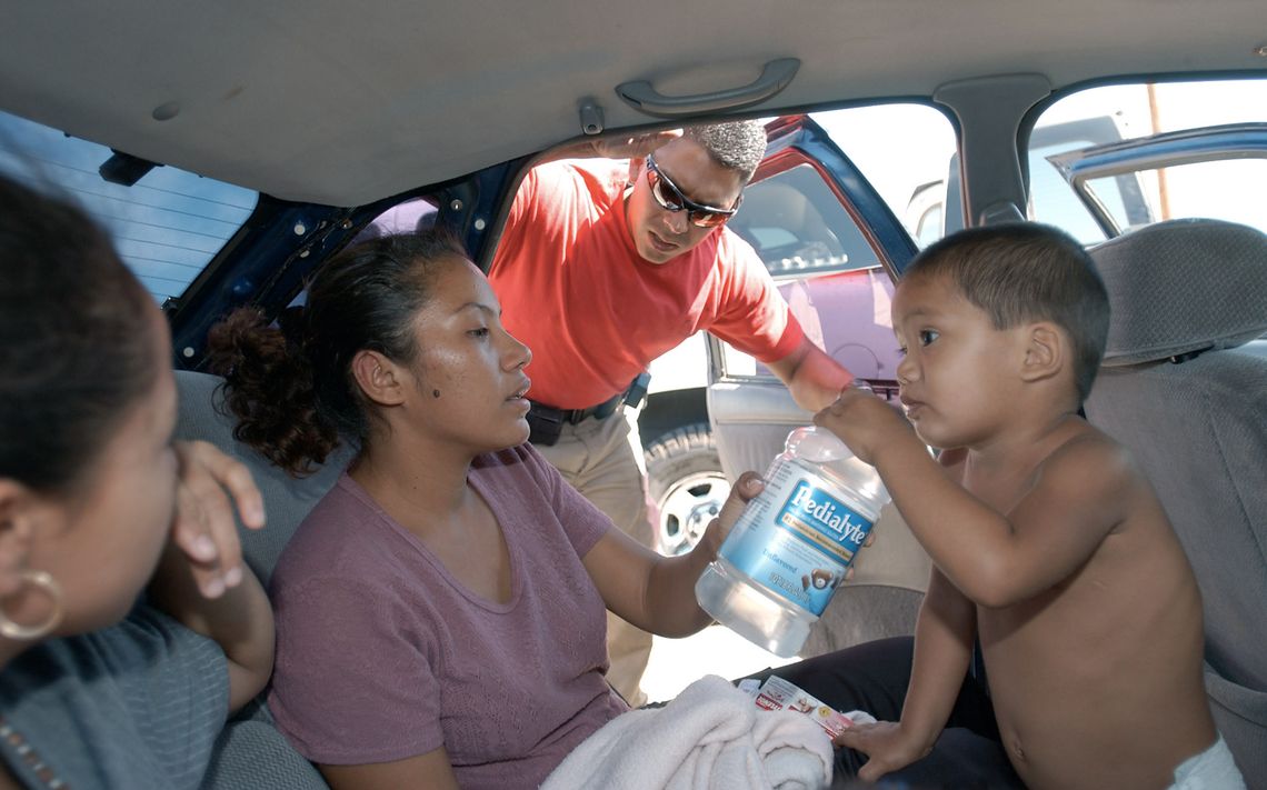 U.S. Border Patrol Search, Trauma, and Rescue (BORSTAR) team member Rick Cardiel watches as a young dehydrated child drinks Pedialyte in the back of a car, near Yuma, in July of 2002.