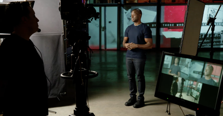 A Black man stands amid cameras and other equipment on the set of a TV show called Inside Story.