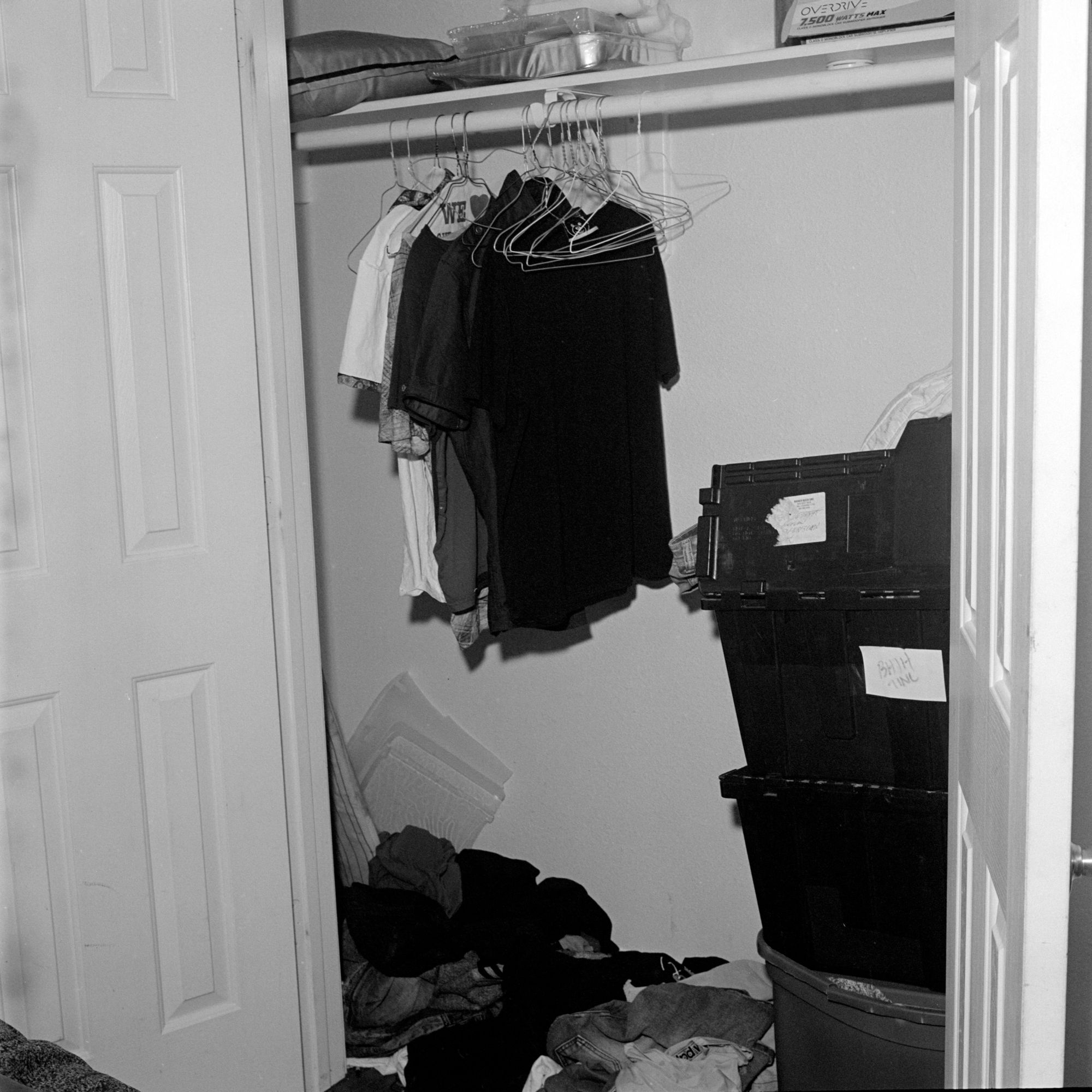 A closet has a few T-shirts hanging in it, and there are a few boxes stacked up. 