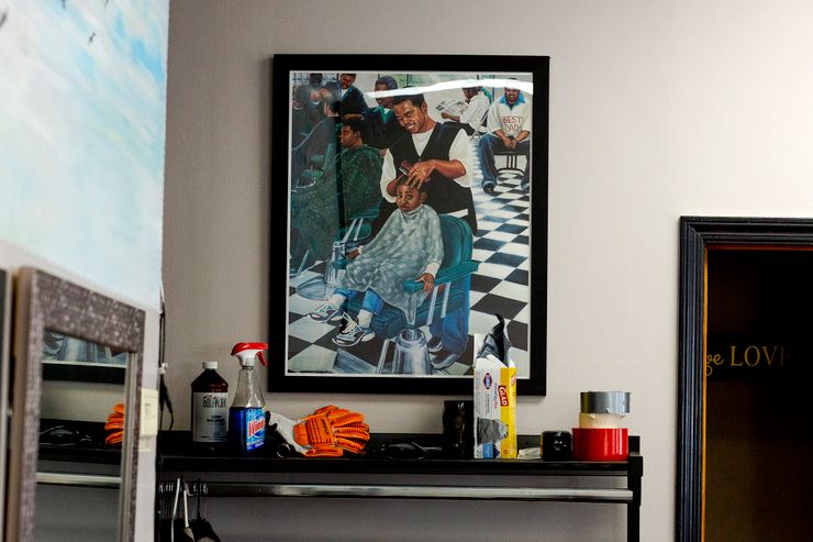 A poster of a Black barber adjusting the head of a Black boy, wearing a cape while he sits on a chair. 