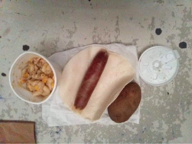 A hotdog with a tortilla, a cup of mush and a raw potato.