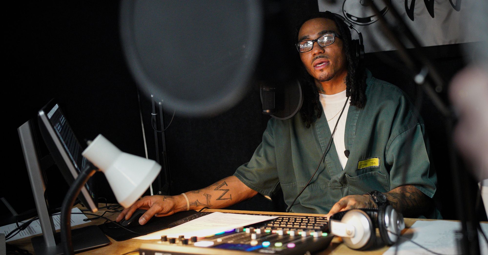 Darrius Turner, a Black man with glasses, works on radio equipment and wears headphones in a studio.  