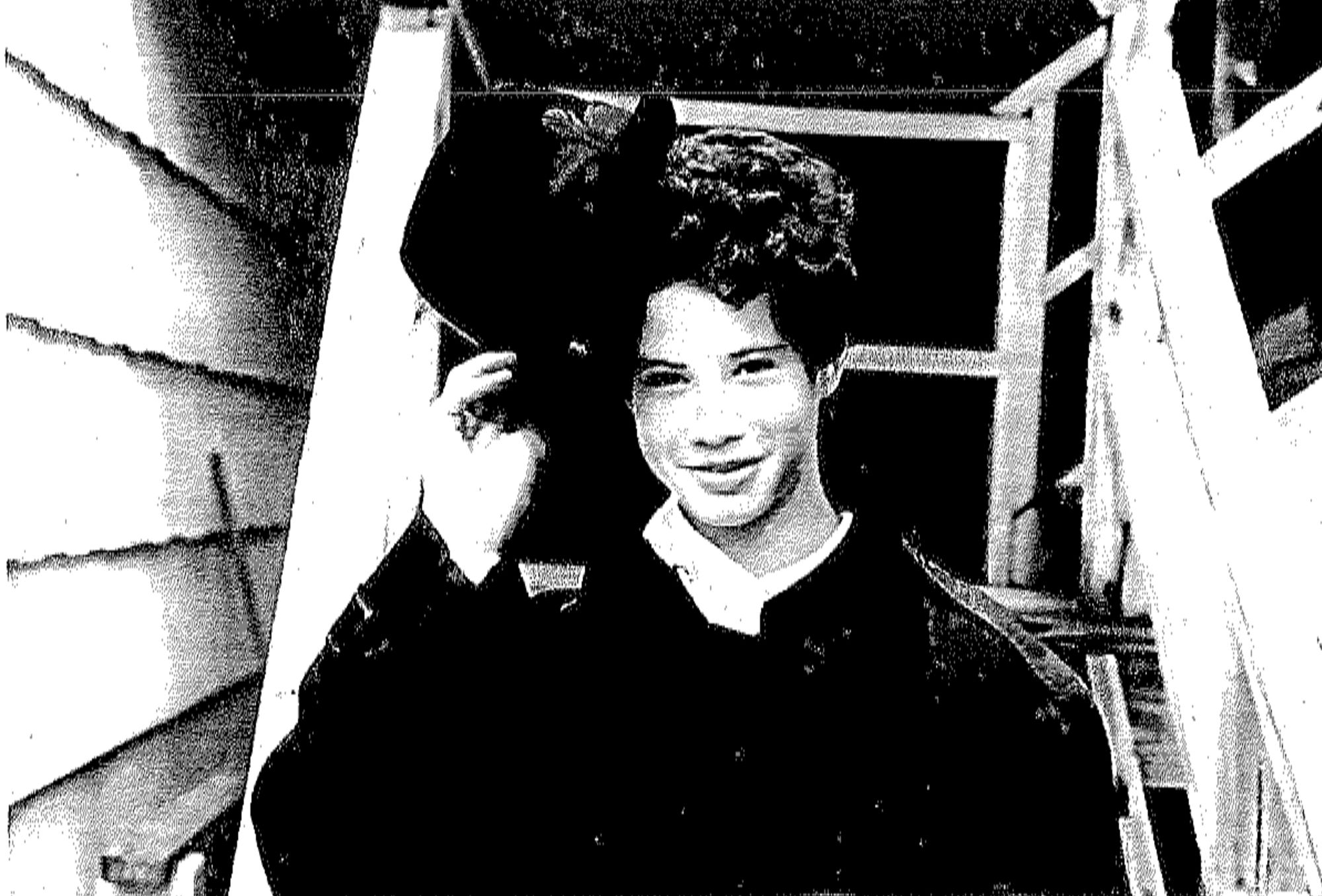 A black and white photocopy of a photo of Eric Kane, a White teenage boy, holding a hat at an angle against his head. 