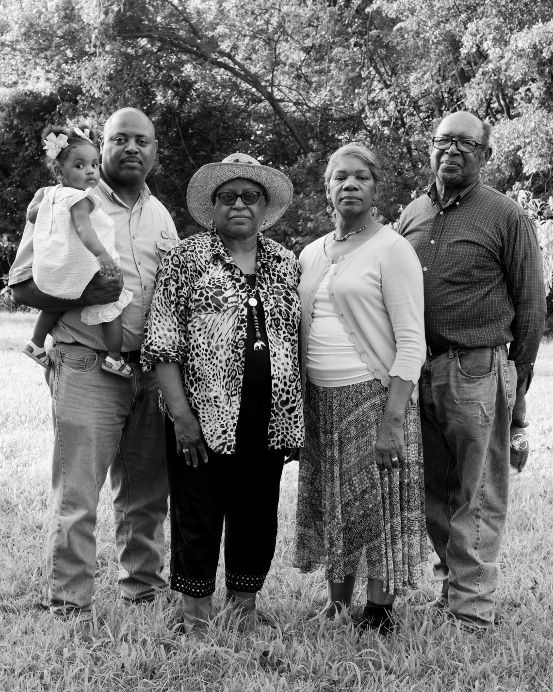 A black-and-white photo shows a Black family posing for a portrait outdoors. 
