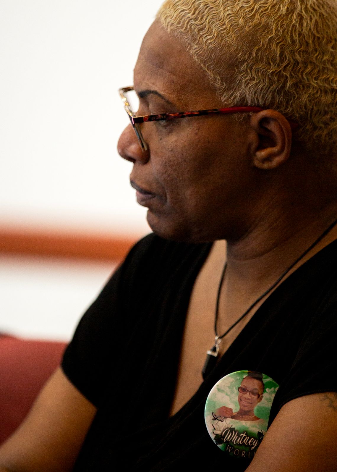 A Black woman with blonde hair wears a button with her daughter’s image on it.