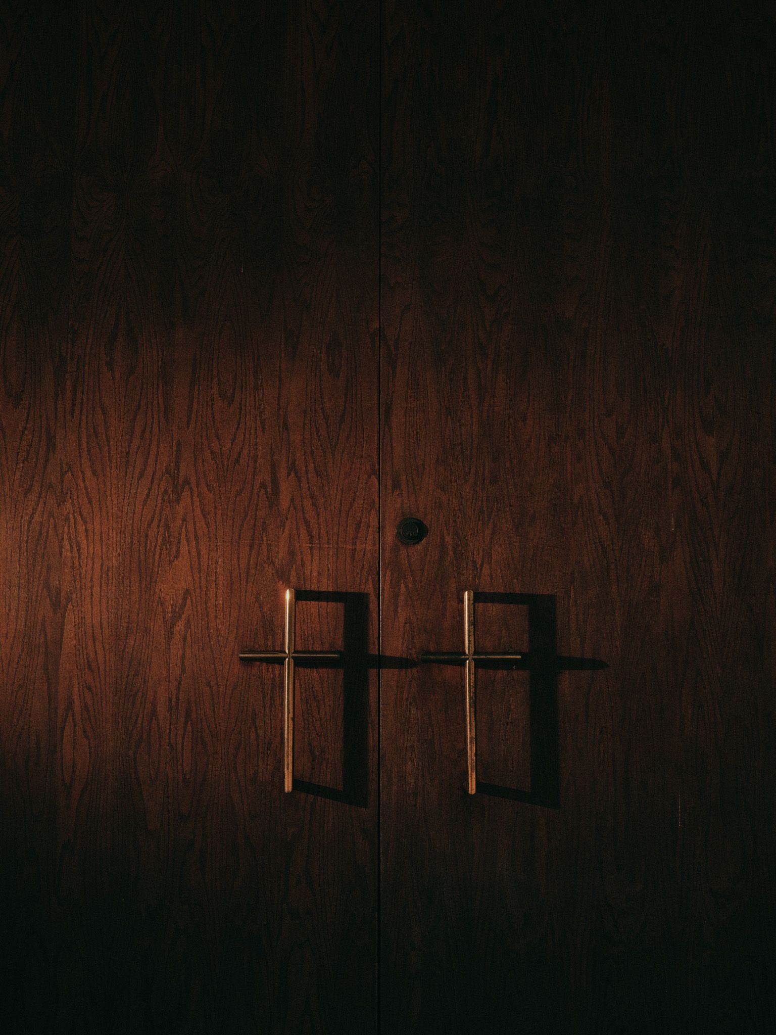 Two wooden doors have door handles that are shaped like thin brass-colored crosses.