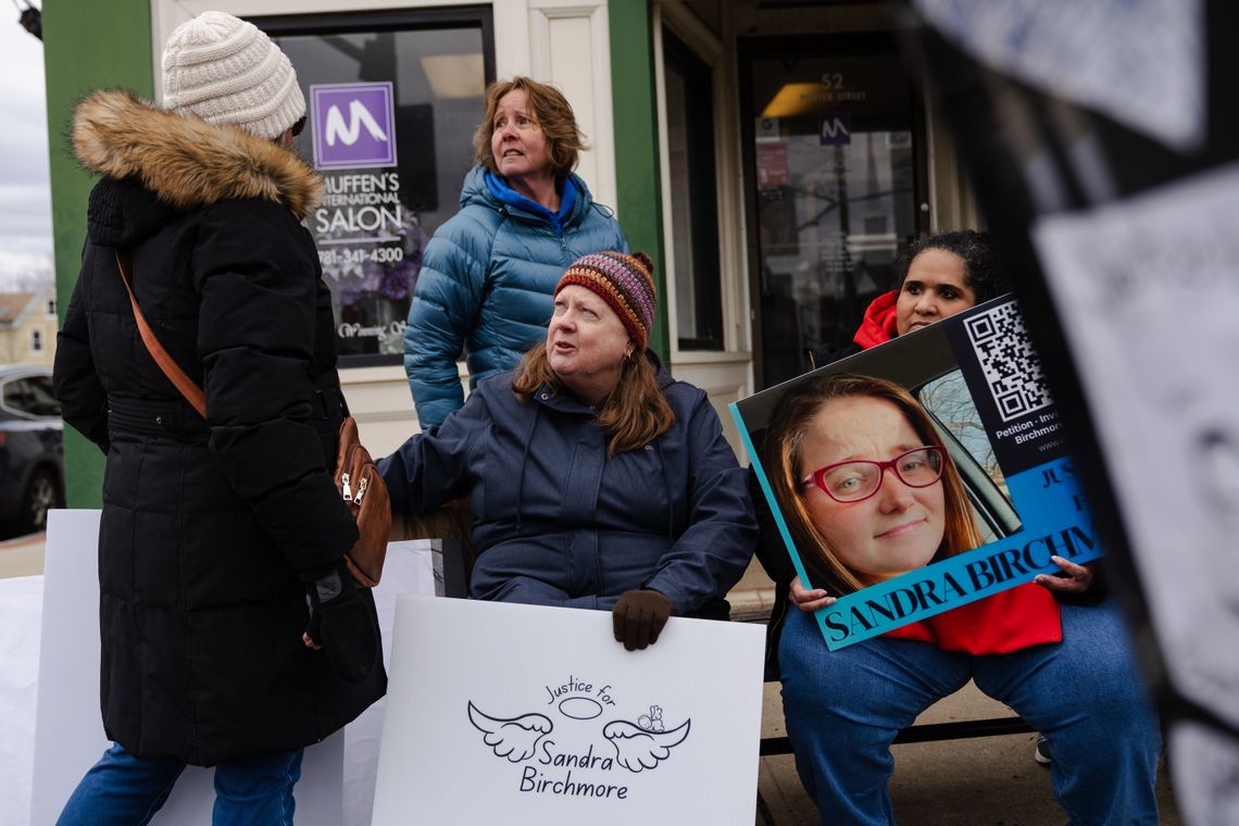 Four people at a protest for Sandra Birchmore, including Sandra's second cousin, Barbara Wright, a White woman with long brown hair, near Stoughton Town Hall. Two people hold signs saying "Justice for Sandra Birchmore."