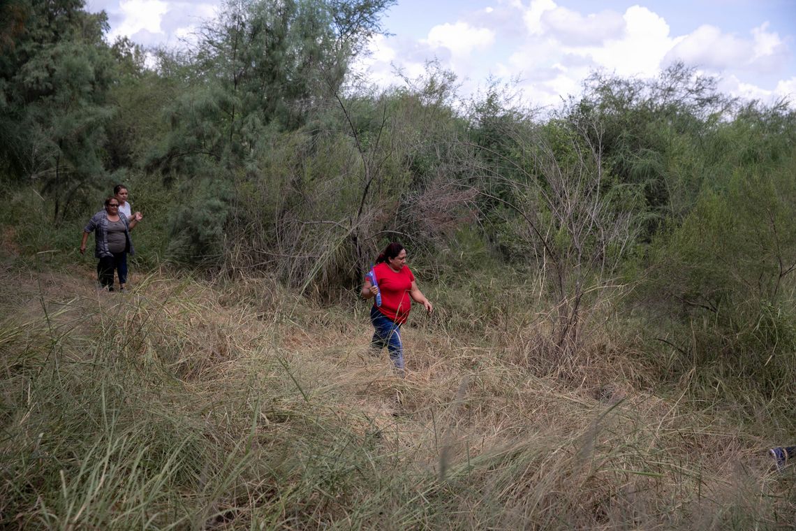 Magda, 45, from Nicaragua (in red), walks near the Rio Grande river after crossing into the United States. A few moments later, she and other family members approached a Border Patrol agent to turn themselves in. 
