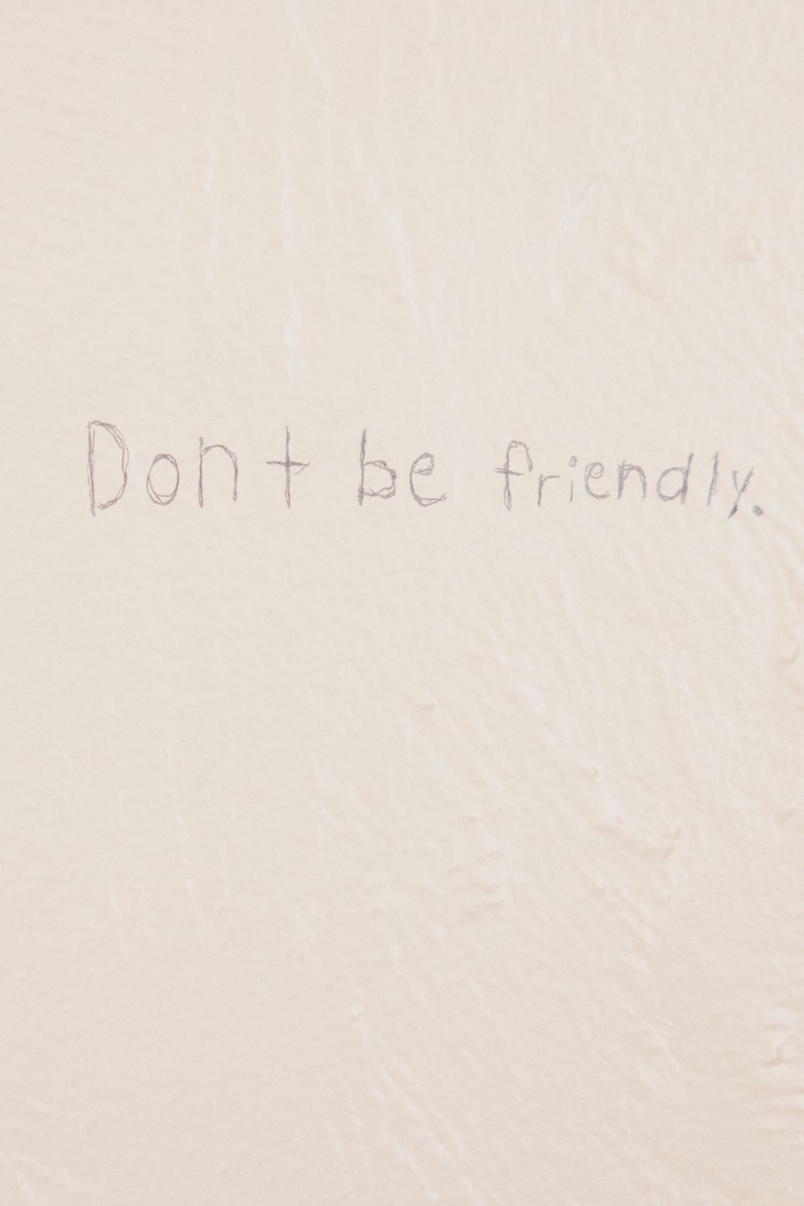 Handwriting on an off-white wall reads "Don't be friendly."