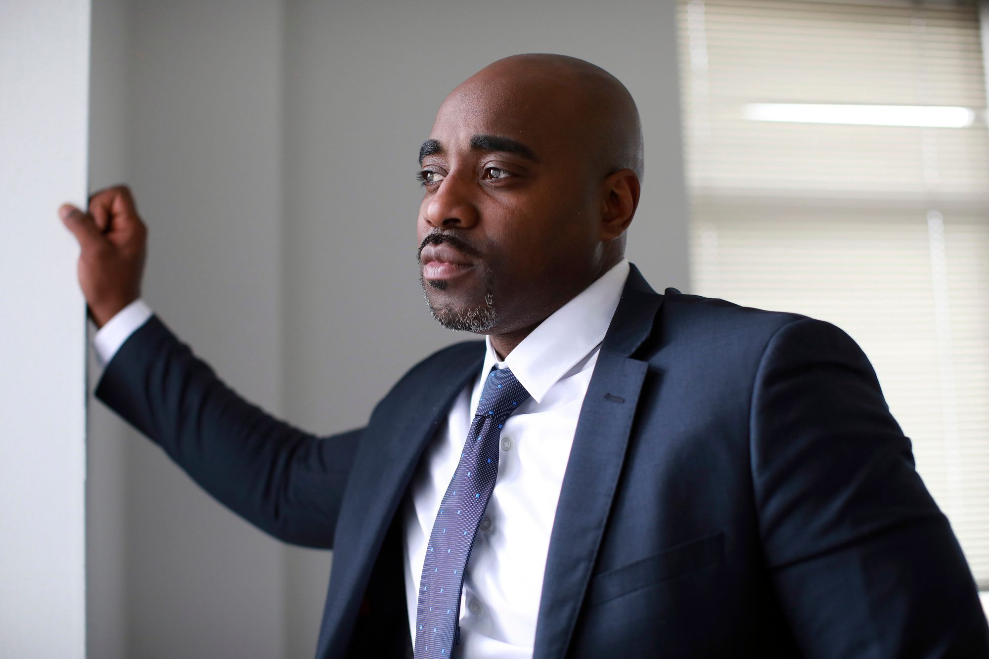 A Black man in a blue suit posing in an office. 