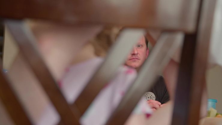 A White man can be seen through the back of a wooden dining-table chair. 