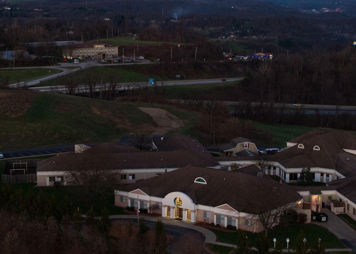 An aerial photo shows a cluster of buildings with grey roofs in a rural setting. A hotel is visible in the distance, on the left.